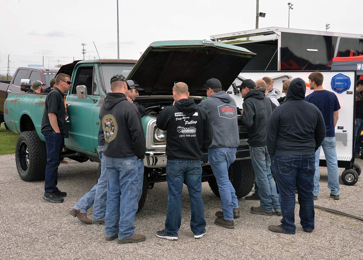 Guys gathered around a truck looking under the hood