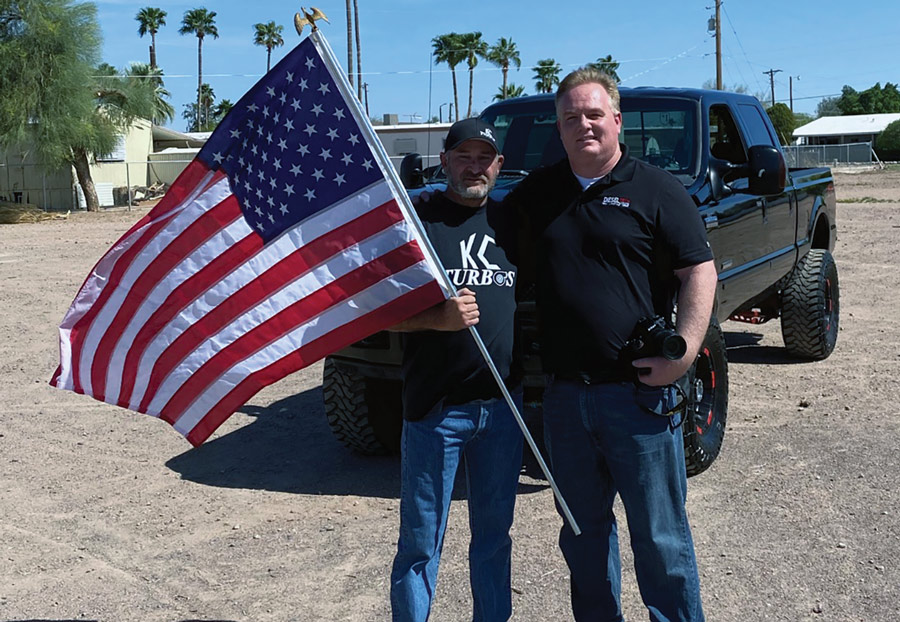 Two men standing side by side with an American flag