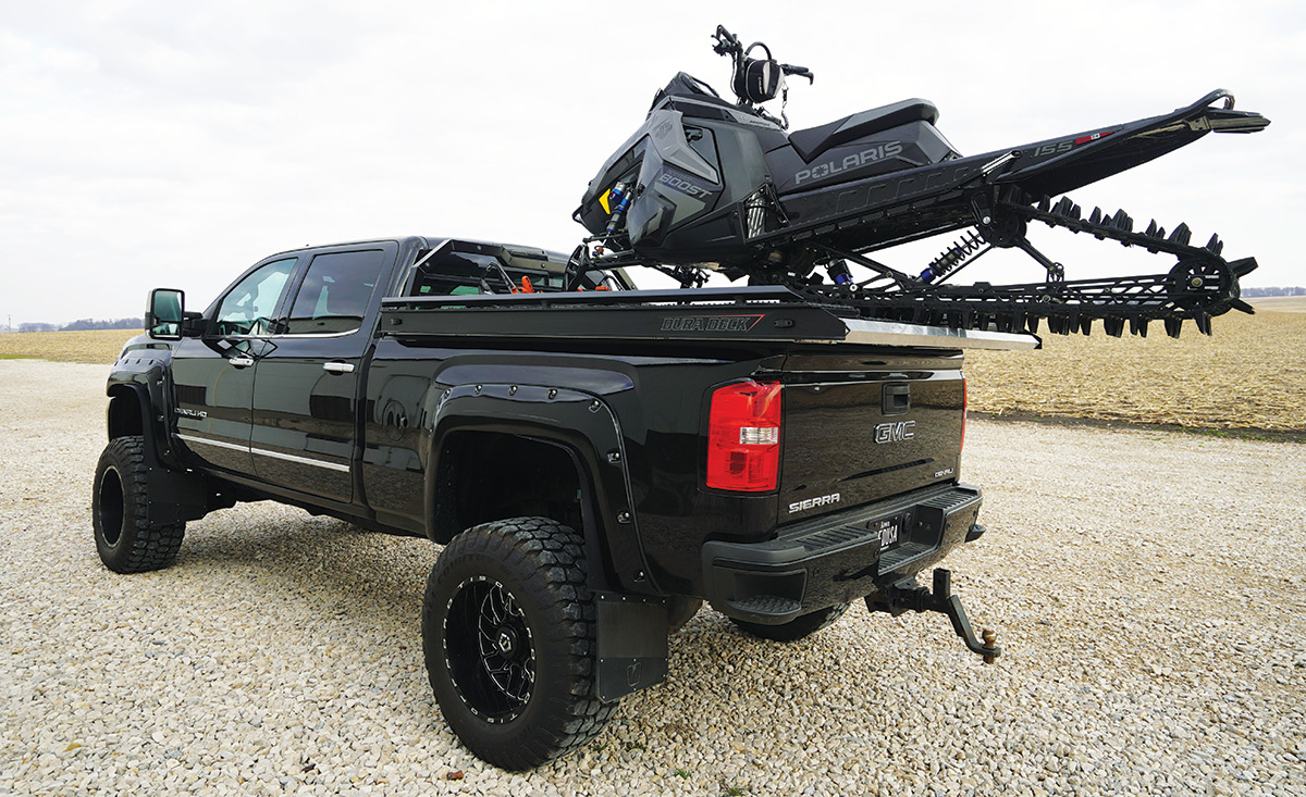 snowmobile hanging over the edge of the 2015 GMC Sierra 2500 trunk