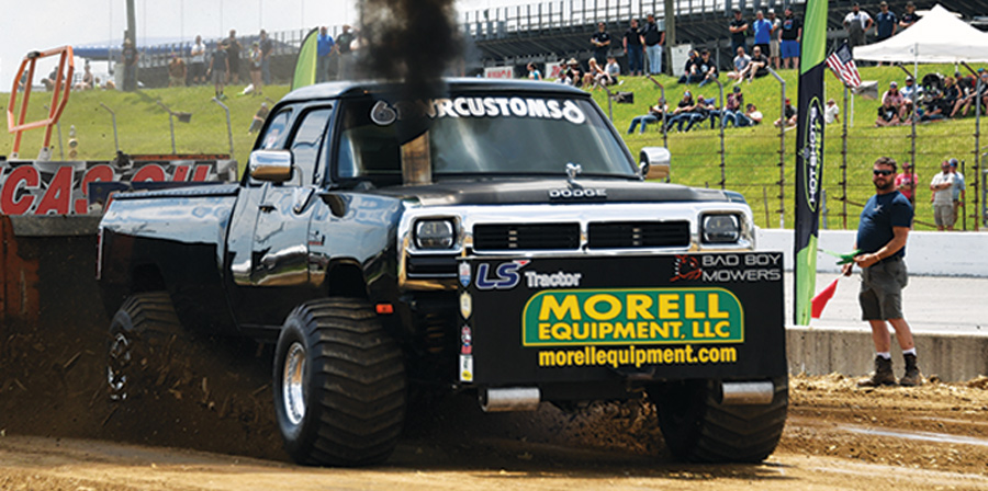 black truck with large tires in a drag race on the dirt