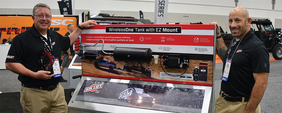 Two representatives from Air Lift stand and smile posing for a picture next to the WirelessOne Tank with EZ Mount product